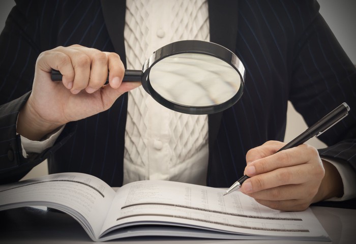 The auditor in the business case examines the financial records through pen and magnifying glass