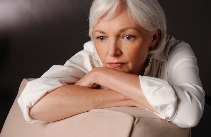 The visible older woman rests her cheek on her folded arms.