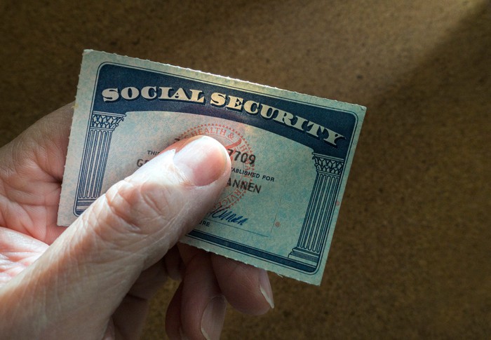 A person grasps a Social Security card between their thumb and forefinger.