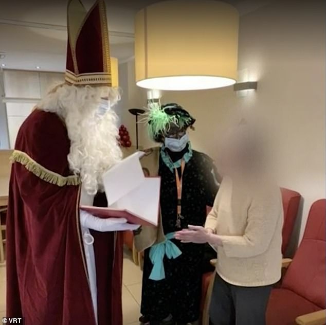 Father Christmas talks to an elderly resident.  She and his assistant stand two meters away from her
