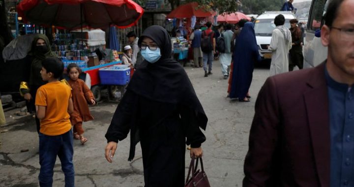 An Afghan woman wearing a mask walks on a street in Kabul