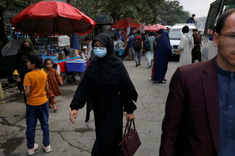 An Afghan woman wearing a mask walks on a street in Kabul